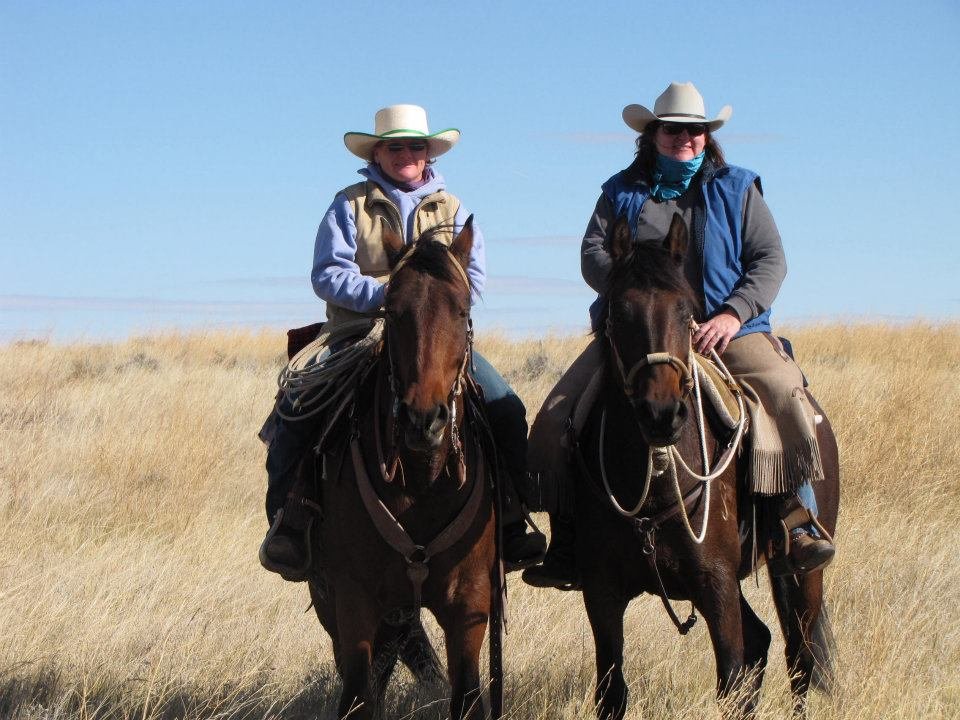 Two cowgirls in cowboay hats and western clothes on bay Morgan horses.